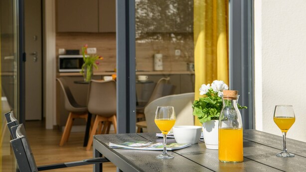 Una mesa de comedor con dos vasos de jugo de naranja, una botella de jugo y un tazón. Se observa una cocina moderna al fondo.