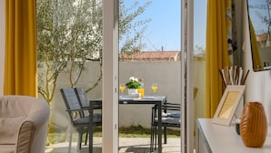 Una habitación con puerta corrediza de vidrio que da a un área exterior con mesa, sillas y un pequeño jardín.