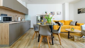 Una cocina moderna con microondas, horno y lavabo. Hay un comedor con mesa y sillas, y un sofá amarillo en la sala de estar.