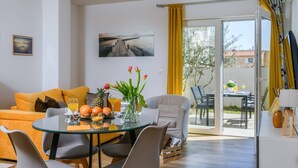 Una sala de estar moderna con una mesa de vidrio, un sofá y una silla. Hay un cuadro en la pared y una ventana con cortinas amarillas.