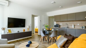 Una sala moderna con un televisor de pantalla plana grande, un sofá, una mesa de centro y un comedor con sillas y una mesa pequeña.
