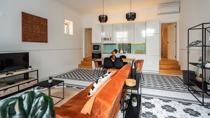 A modern living room with a sofa, TV, and a dining area with chairs and a table. - Ruby Orange Apartment, WiFi, AC !New! (Lisboa)