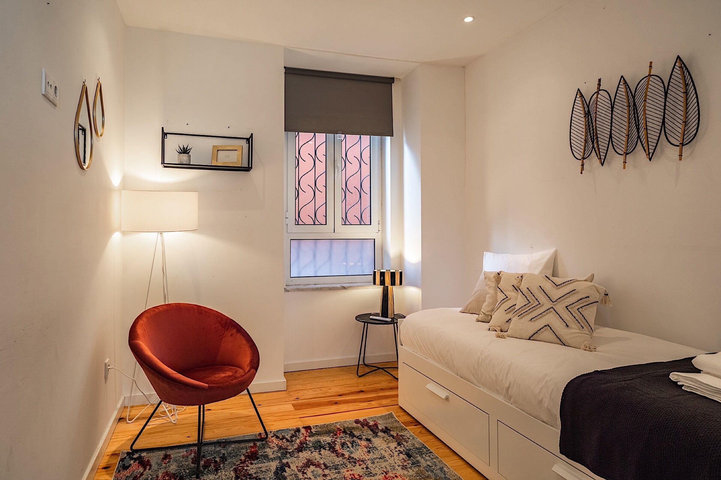 Un dormitorio con cama, una silla, una ventana con cortina, una mesita de noche y adornos en la pared.