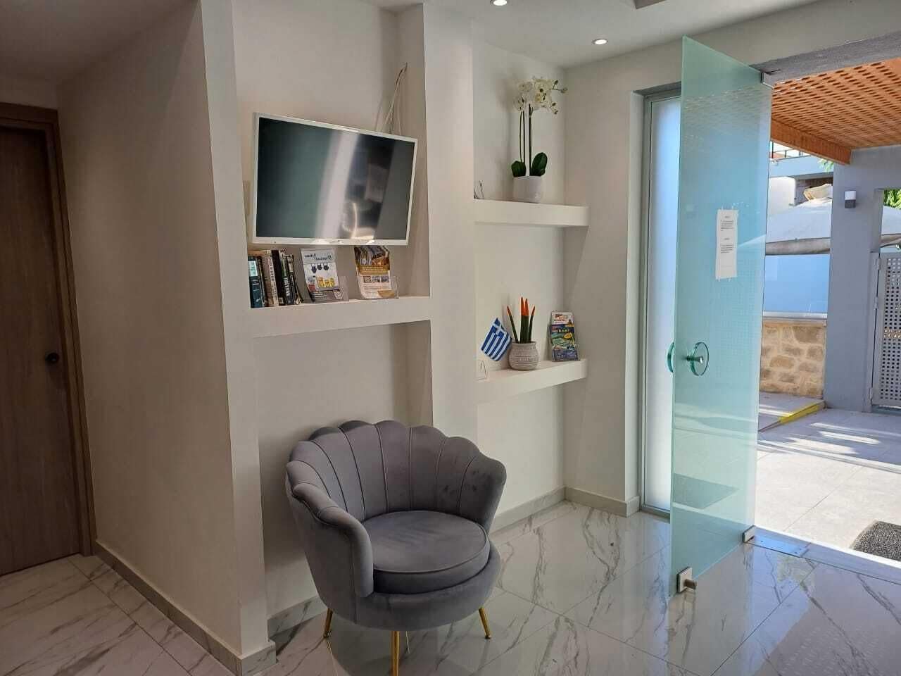 A reception area with a grey armchair, a flat-screen TV, and a glass door leading outside.