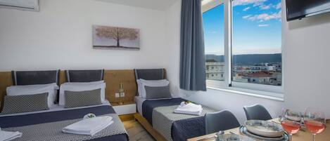 A hotel room with two beds, a dining table with plates and glasses, and a view of the city through large windows.