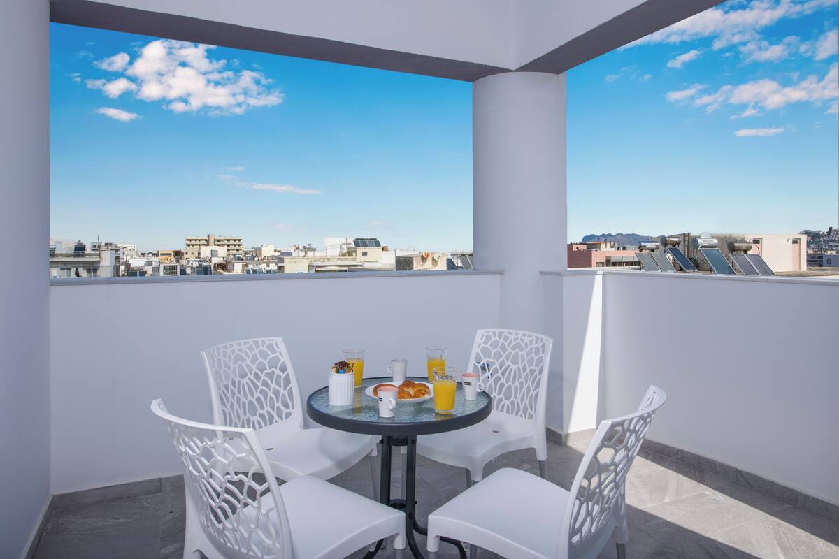 A balcony with a table and chairs, a glass of orange juice, and a view of the cityscape.
