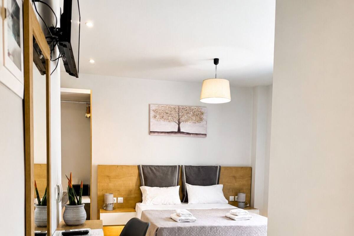 A modern hotel room with a bed, bedside tables, a desk, a chair, a lamp, and a painting on the wall.