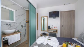 A hotel room with a bathroom, a bed with towels, a tray with drinks, and a TV. - Deluxe City (Chania)
