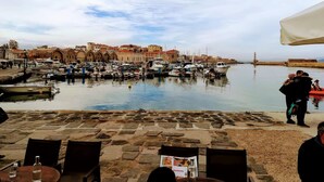 A harbor with boats, stone buildings, and a clear sky. - Deluxe City (Chania)