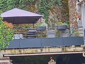 A rooftop terrace with a covered seating area, air conditioning units, and a stone wall backdrop.