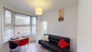 A modern living room with a black leather sofa, a dining table with chairs, and a painting of the Eiffel Tower. - The Rock Apartments II (London)