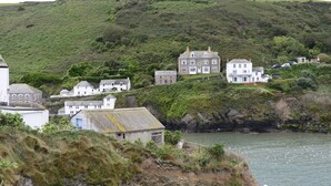 Un pueblo costero con casas de piedra tradicionales, un litoral rocoso y una colina al fondo.