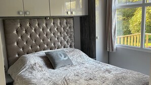 Un dormitorio con cabecera capitonada, cama con colcha estampada y vista a una terraza de madera a través de una ventana.