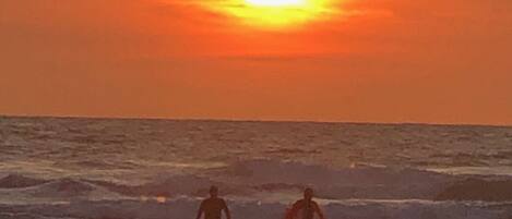 Two people standing on a beach at sunset.