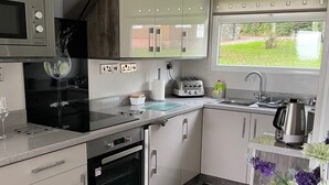 Cocina compacta con microondas, tostadora y horno. Se ve un ventanal con vistas a zonas verdes.