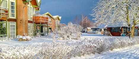 A snow-covered landscape with buildings, including a brick structure with large windows and a green roof.