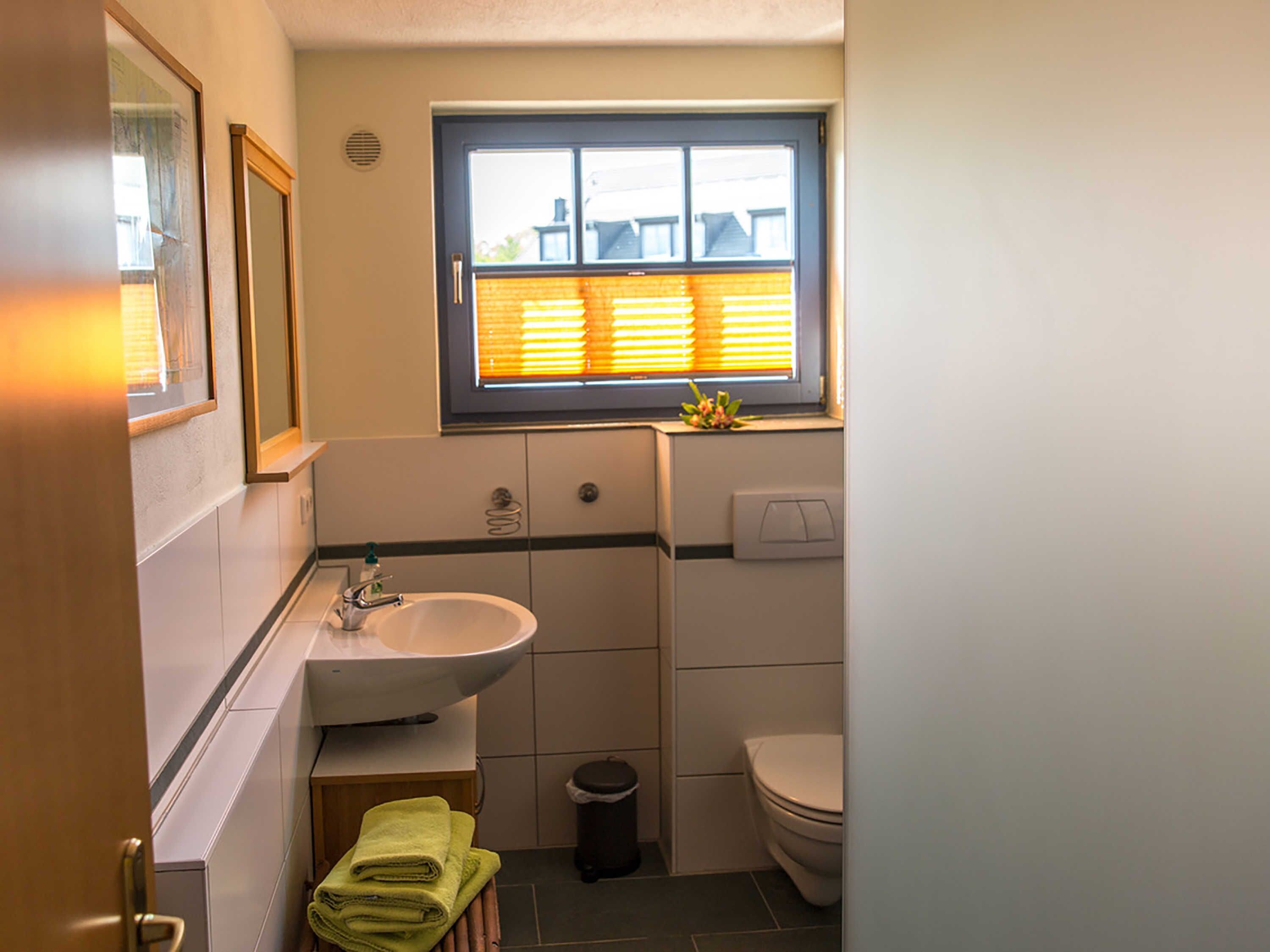 A bathroom with a sink, toilet, window, and a small trash bin.