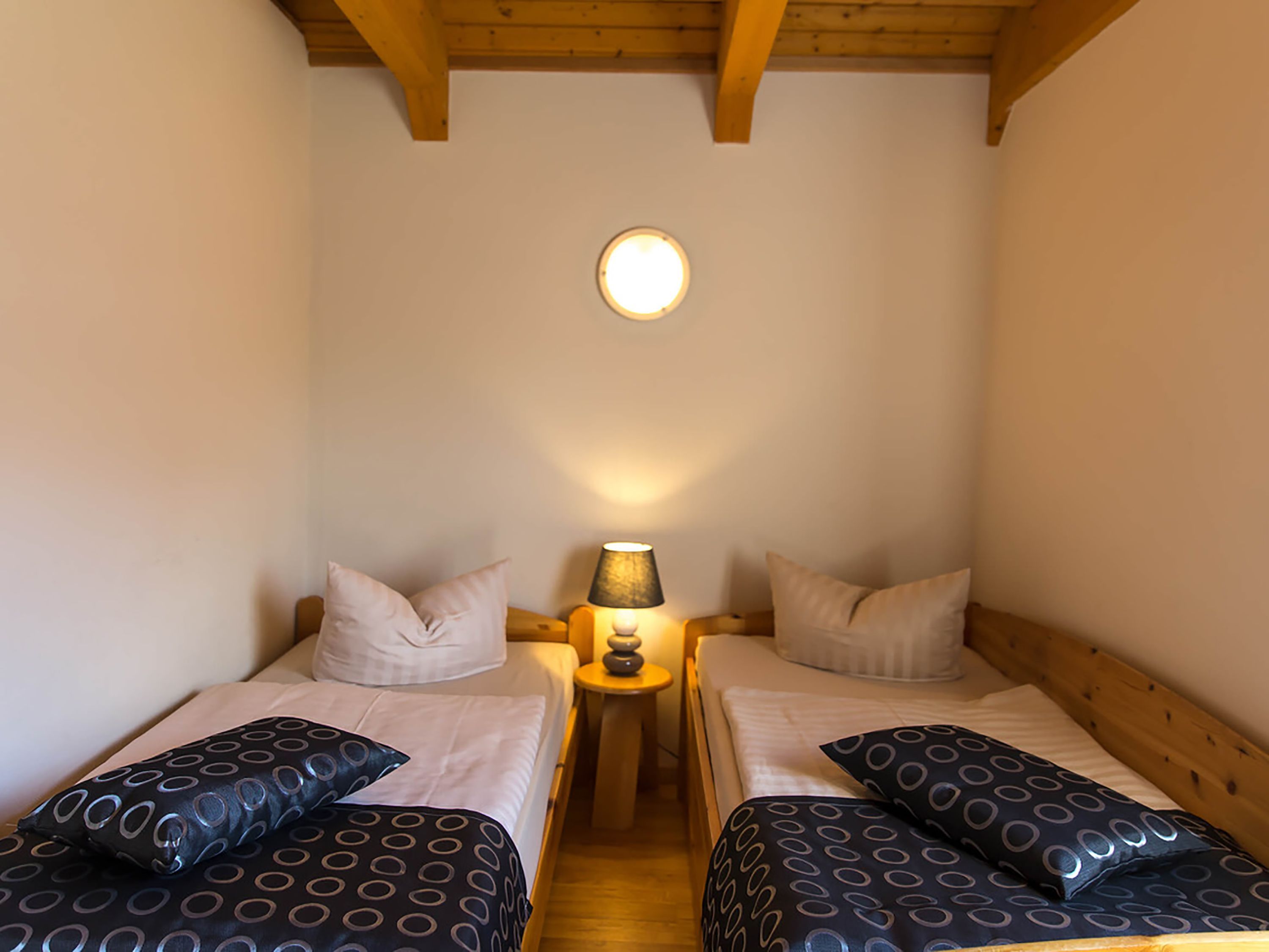 Une petite chambre agréable, dotée de deux lits simples, d’une table de chevet avec une lampe et d’un luminaire au plafond.