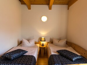 Een knus kamertje met twee eenpersoonsbedden, een nachtkastje met lamp en een plafondlamp.