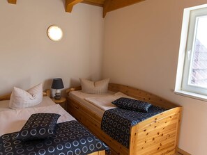 Een kamer met twee houten bedden, een nachtkastje met een lamp, een ronde wandlamp en een raam.