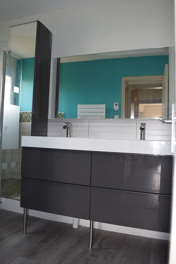 Une salle de bain moderne avec un grand miroir, un lavabo blanc et un meuble-lavabo foncé.