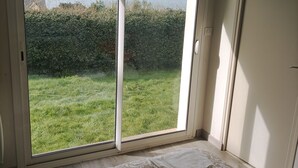 Una habitación con un amplio ventanal corredizo que da a un espacio al aire libre con césped y vistas al mar.