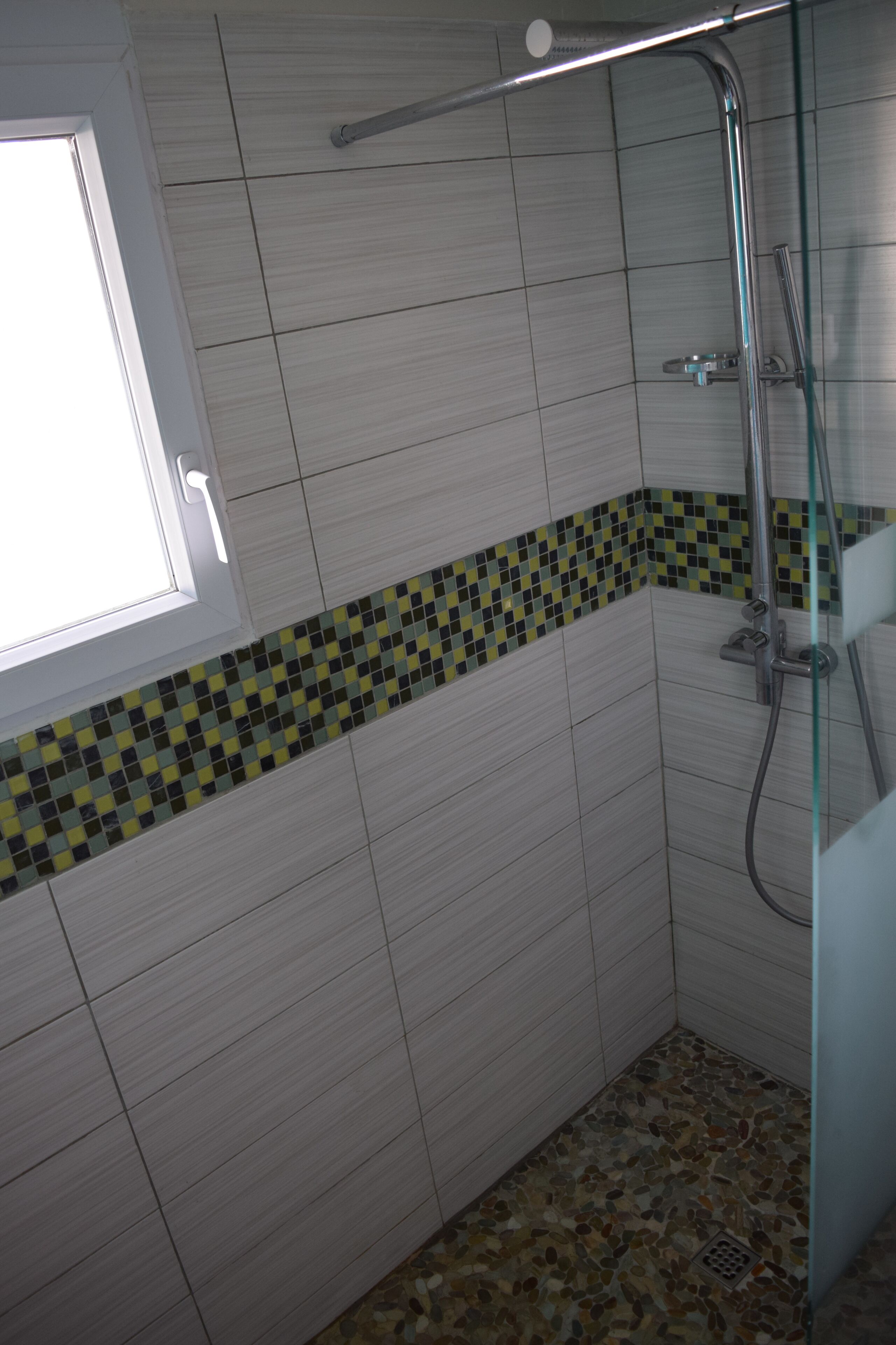 Une salle de bain avec des carreaux blancs, une bordure à motifs à carreaux et un espace douche.