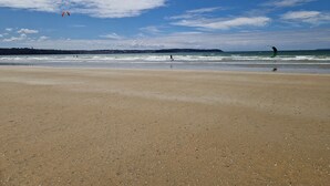 Una playa con cielo despejado y algunos cometas volando.