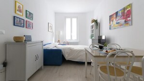 A compact, modern room with a bed, a desk, and a chair. There are framed pictures on the wall and a window providing natural light. - HouSmart Vicolo Bolognetti (Bologna)