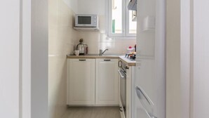 A compact kitchen with white cabinets, a microwave, a sink, and a window above the counter. - HouSmart Vicolo Bolognetti (Bologna)