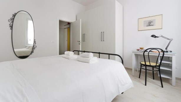 A bedroom with a bed, a desk, a chair, a mirror, and a door leading to another room. - HouSmart Vicolo Bolognetti (Bologna)