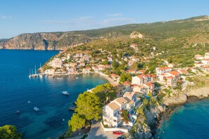 A coastal village with houses along the shoreline, a marina with boats, and a hilly backdrop.