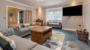 Un salon moderne avec un canapé gris, une table basse en bois et un téléviseur à écran plat fixé au mur.