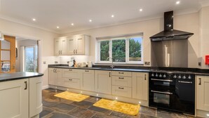 Une cuisine moderne avec des meubles blancs, une cuisinière noire et une fenêtre donnant sur la forêt.