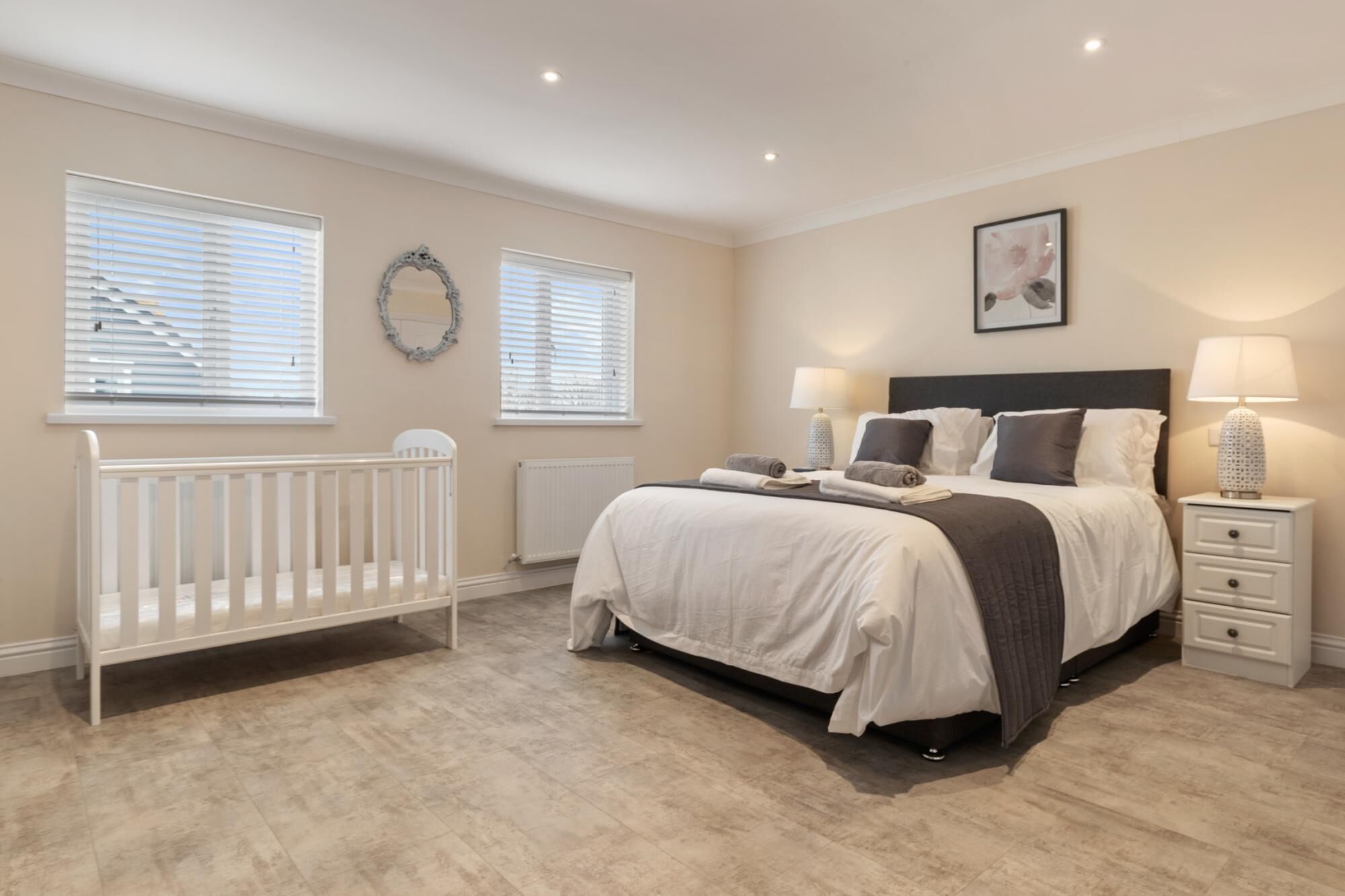 Une chambre à coucher avec un berceau, un lit avec une tête de lit, des tables de chevet et un miroir fixé au mur.
