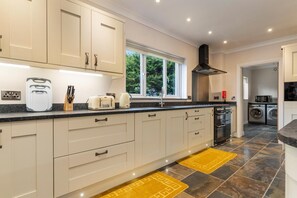 A modern kitchen with white cabinets, a black countertop, and a window with a view of greenery. - Maynor - Large Luxury House Log Burner Central Location (Kilgetty)