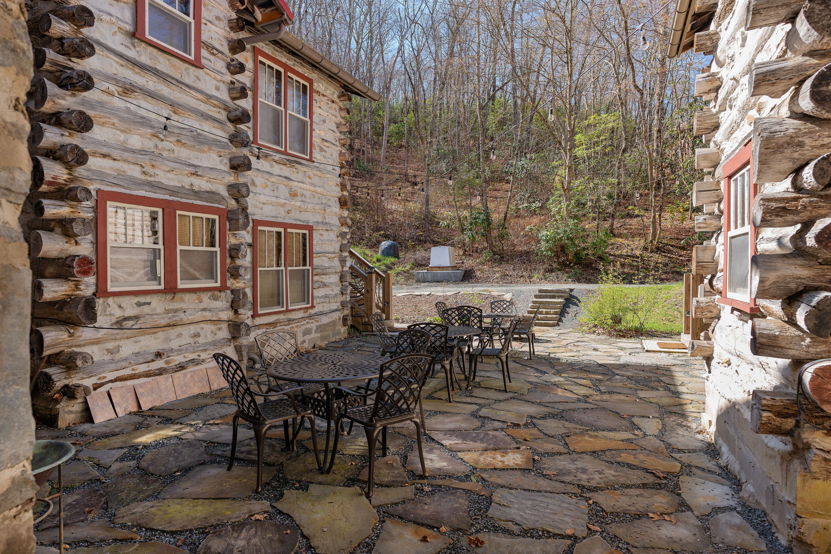 A log cabin with a stone patio, outdoor seating, and a forest backdrop.