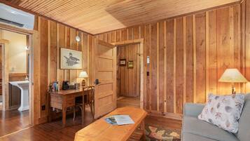 A wooden-paneled room with a wooden desk, a bench, a sofa, and a lamp.