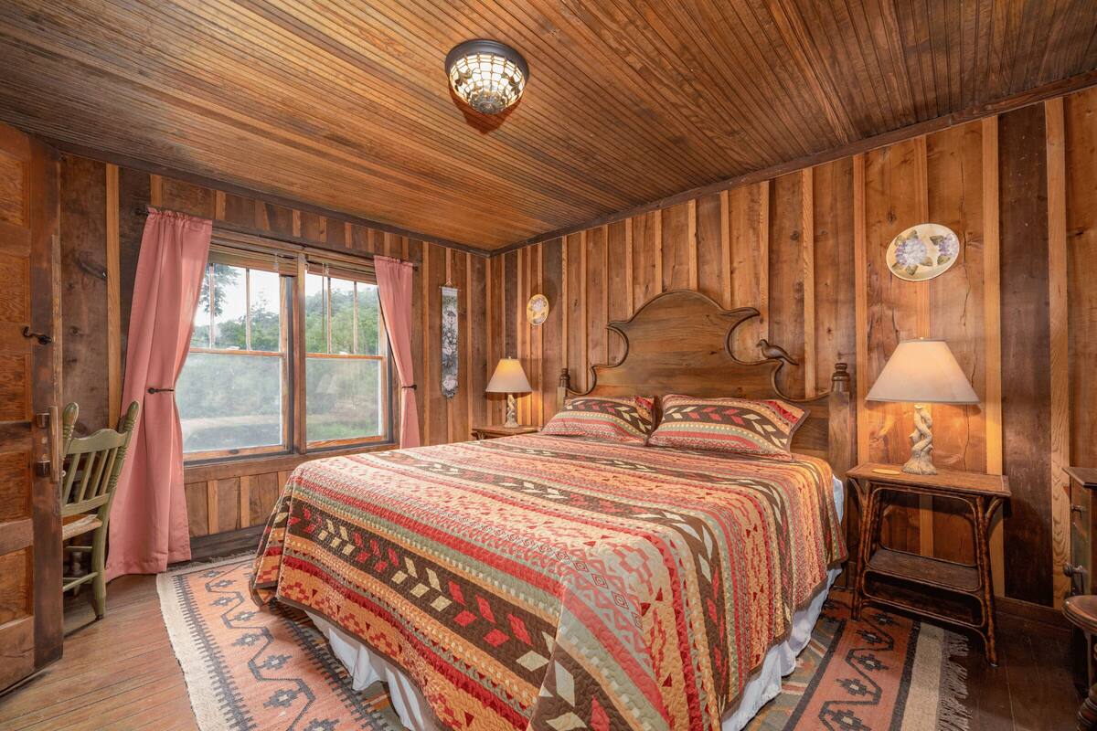A wooden-paneled bedroom with a large bed, two bedside lamps, and a window with curtains.