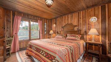 Un dormitorio con paneles de madera, una cama grande, dos lámparas de noche y una ventana con cortinas.