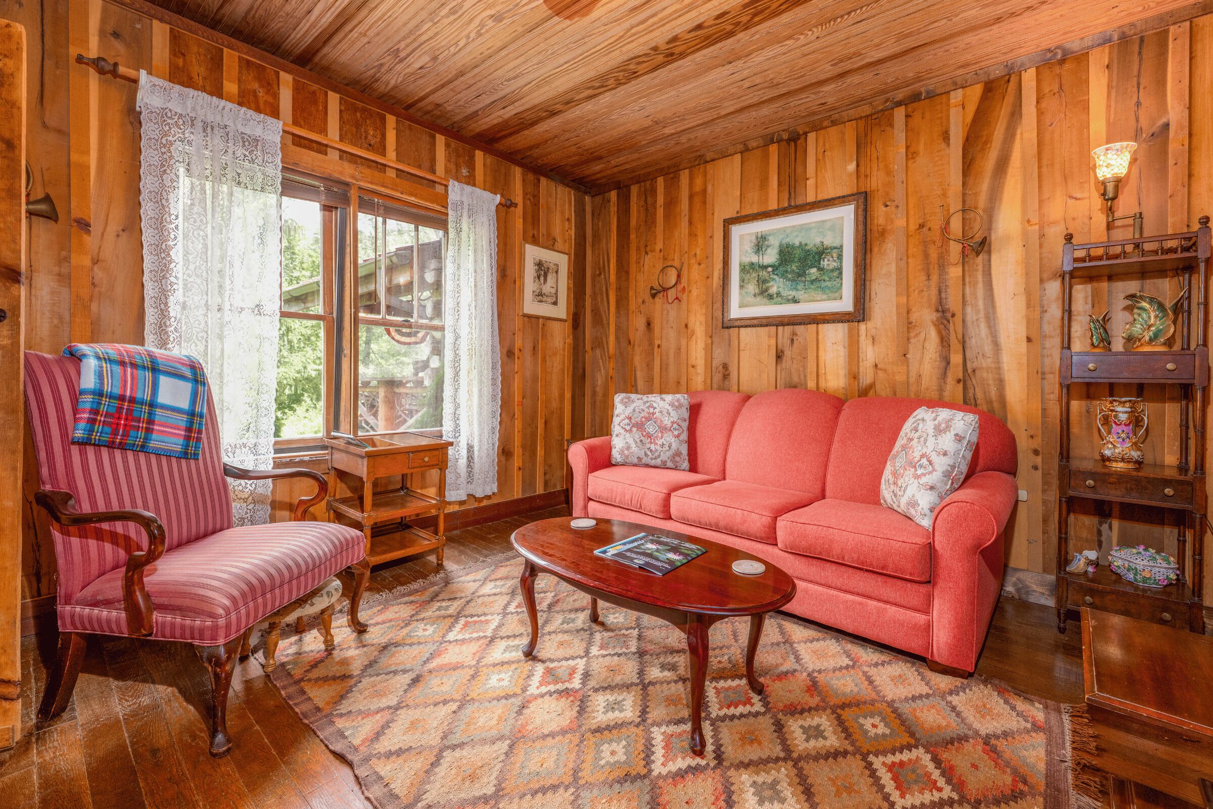 A wooden-paneled room with a red sofa, a striped chair, a wooden coffee table, and a patterned rug.
