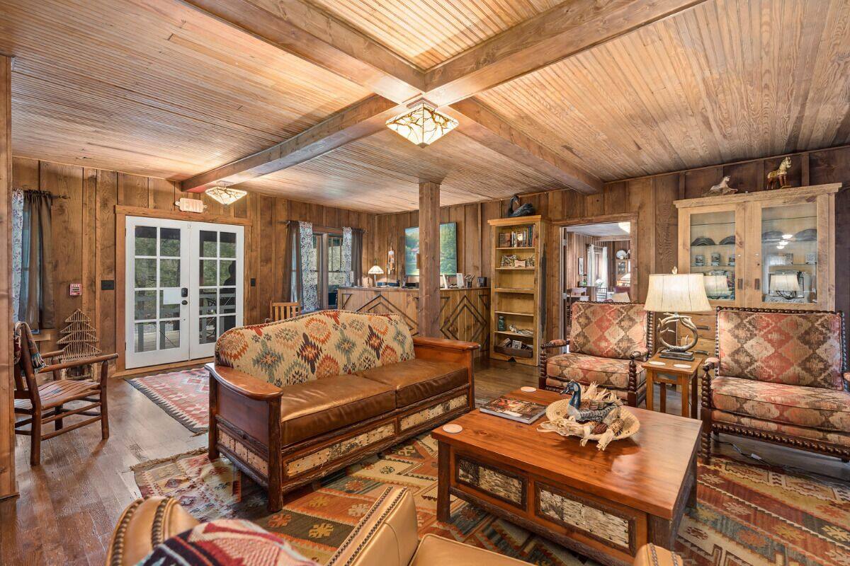 A cozy living room with wooden walls and floors, a sofa, armchairs, a coffee table, and a bookshelf.