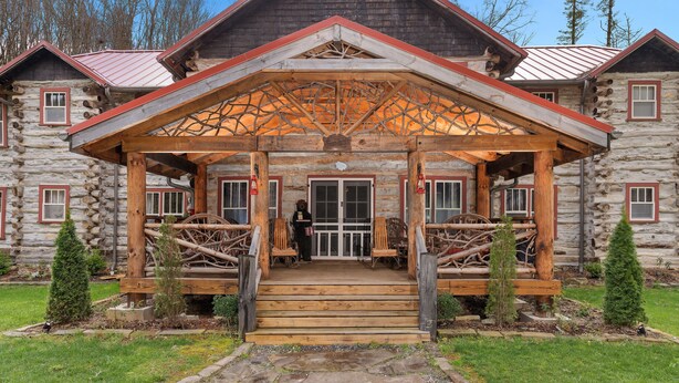 A log cabin with a wooden porch, stone pathway, and a small garden with evergreen trees. - Glen Choga Lodge (Topton)