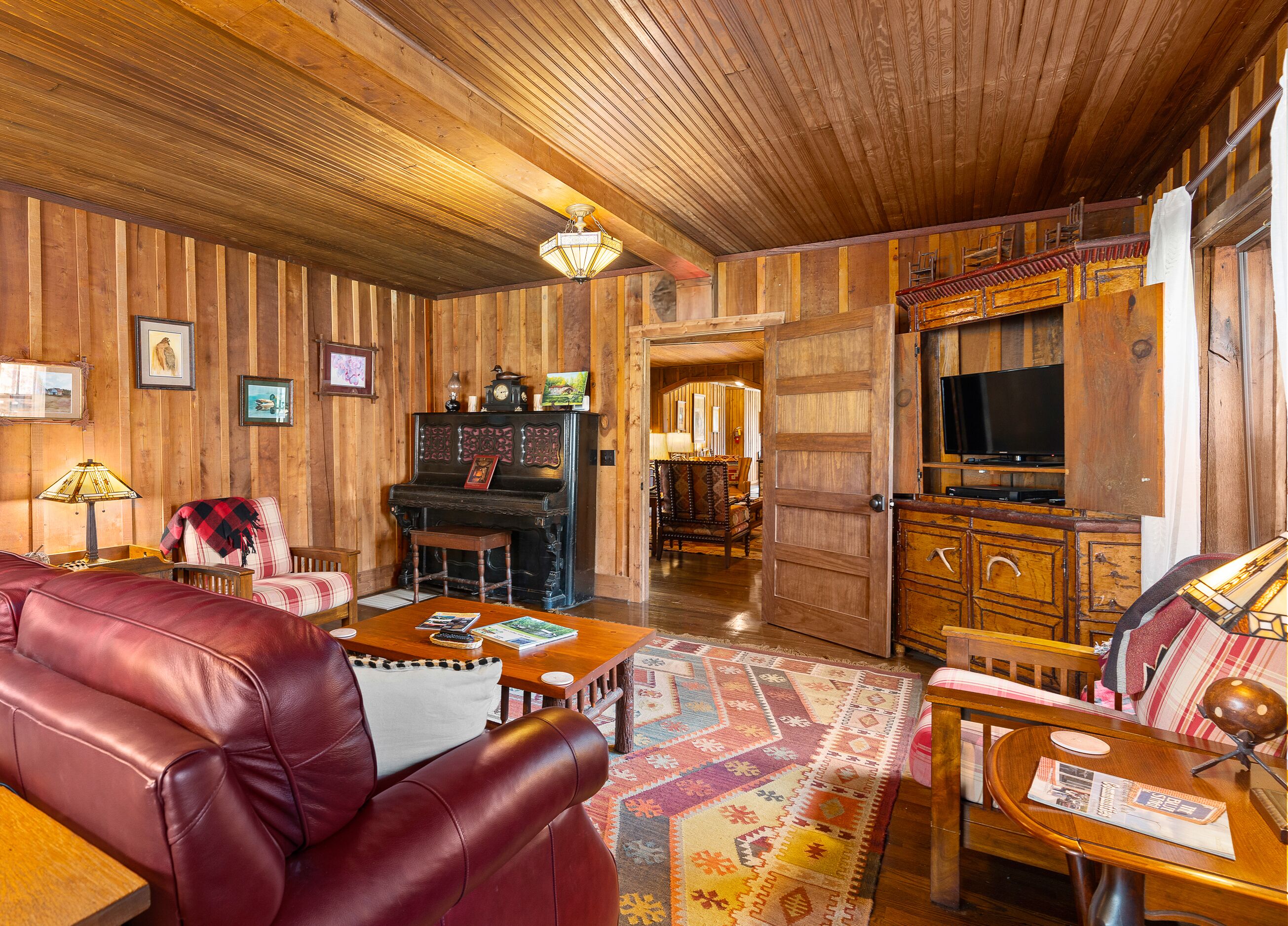 A cozy living room with a wooden interior, a piano, a television, and a leather sofa.