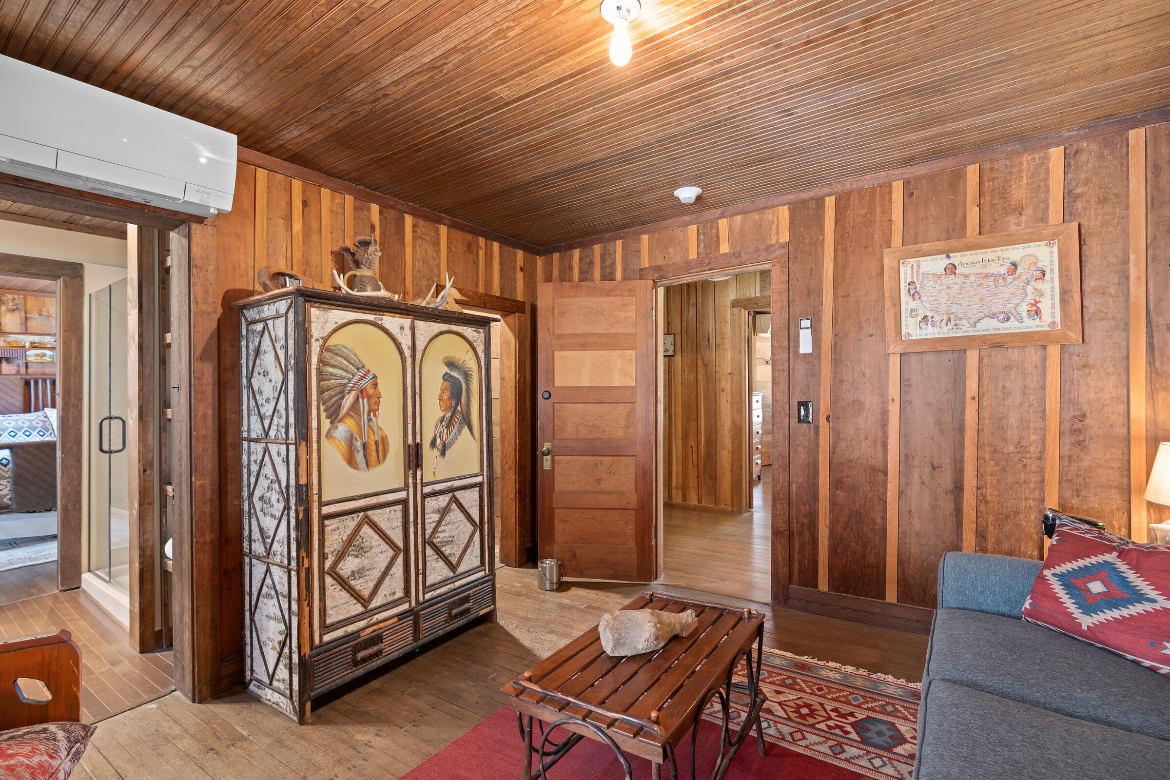A room with wooden paneling, a large cabinet with artwork, a sofa, and a table.