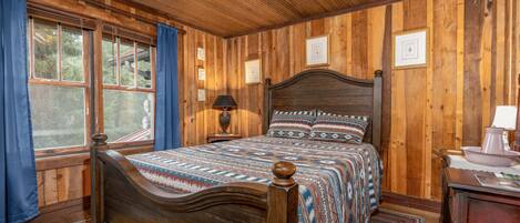 Een slaapkamer met houten lambrisering, een bed, nachtkastje, lamp en raam met gordijnen.