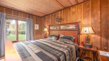 A wooden-paneled bedroom with a large bed, two bedside tables, and a view of the outdoors.