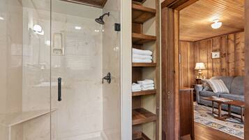 A bathroom with a glass-enclosed shower, wooden shelving with towels, and a wooden ceiling.