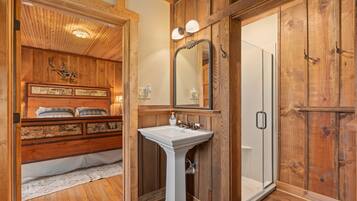 Un baño de madera con lavamanos pedestal, un espejo y una ducha.