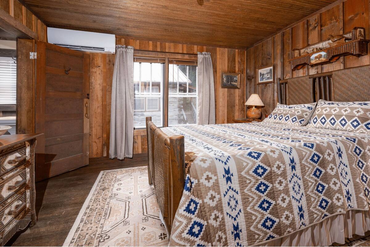A wooden room with a bed, a dresser, and a window with curtains.